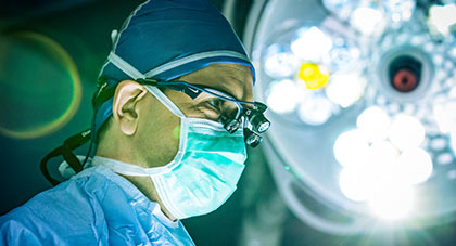 AHN surgeon wearing surgical mask, cap, and gown under bright lights